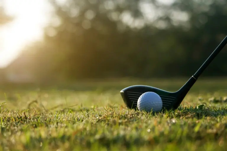 Golf ball beside a driver on a sunlit golf course