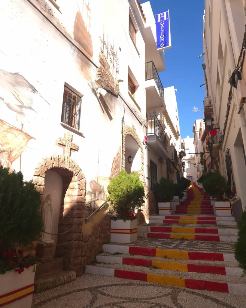 Spanish flag steps beside painted murals in Calpe Old Town