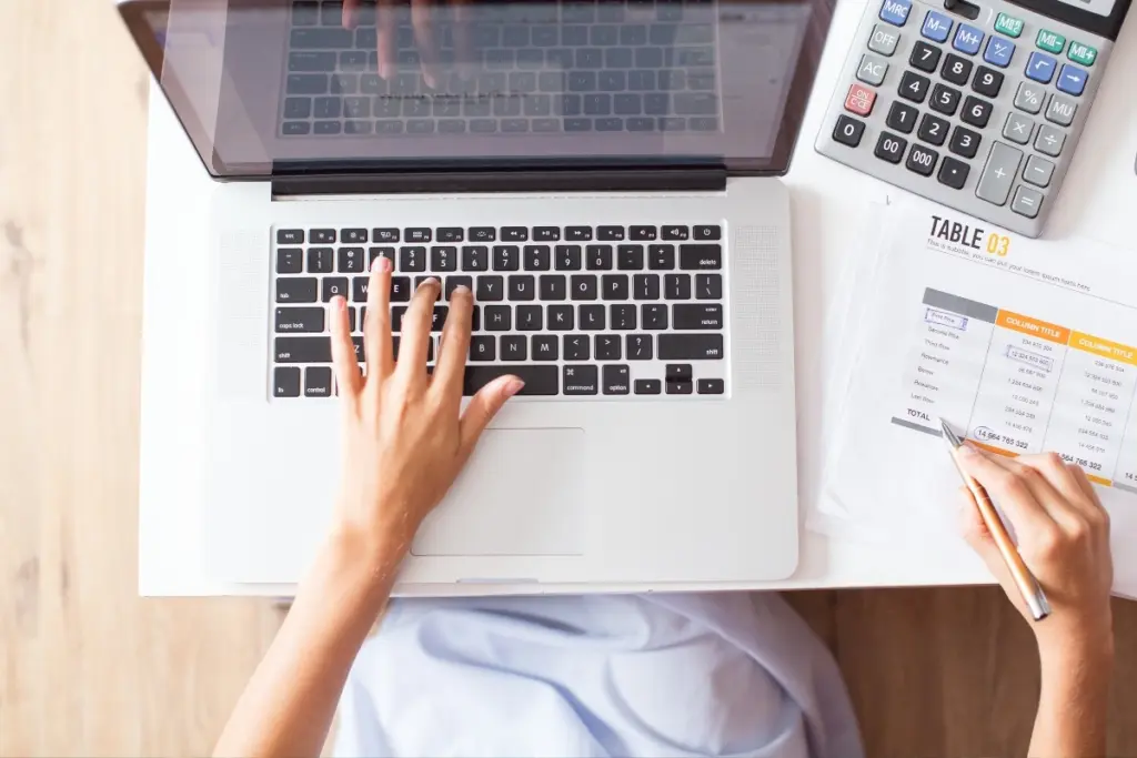 Person completing financial paperwork beside a laptop and calculator